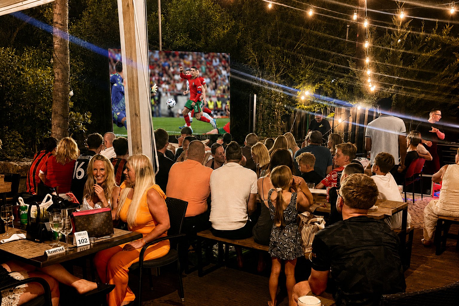 A packed Oscars terrace watching football on the big outdoor screen at night